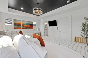 Ein modernes Schlafzimmer mit einem großen Bett, einer Kronleuchter, Kunstwerken an der Wand und einem Fernseher.