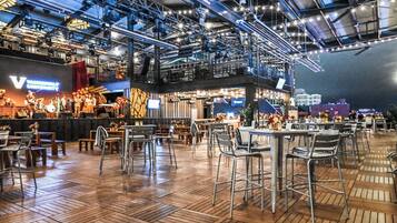 Un comedor interior con mesas y sillas, un escenario con una banda y un techo alto con vigas a la vista.