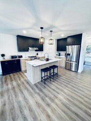 A modern kitchen with dark cabinets, stainless steel appliances, and a central island with stools. - La Belle Montagne- Luxury Ski & Spa (saint côme)