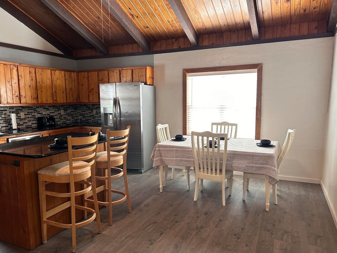 A kitchen with wooden cabinets, a refrigerator, and a dining area with a table and chairs.
