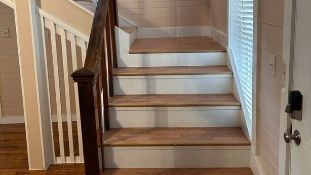A staircase with wooden steps and a wooden handrail, leading to a landing with a white door and a window with blinds. - Garfield Place — Your Nature Escape Awaits! (Alpine)