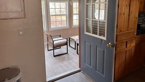 A room with a door leading to a patio area with a chair and table. - Garfield Place — Your Nature Escape Awaits! (Alpine)