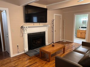 Ein Wohnzimmer mit Kamin, einem flachbildfernseher darüber, einem Couchtisch aus Holz und einer Couch.