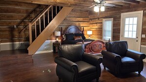 A wooden interior with a staircase, two leather armchairs, a bed, and a ceiling fan. - Garfield Place — Your Nature Escape Awaits! (Alpine)