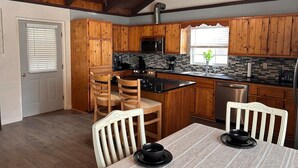 A kitchen with wooden cabinets, a black countertop, and a dining table with chairs. - Garfield Place — Your Nature Escape Awaits! (Alpine)