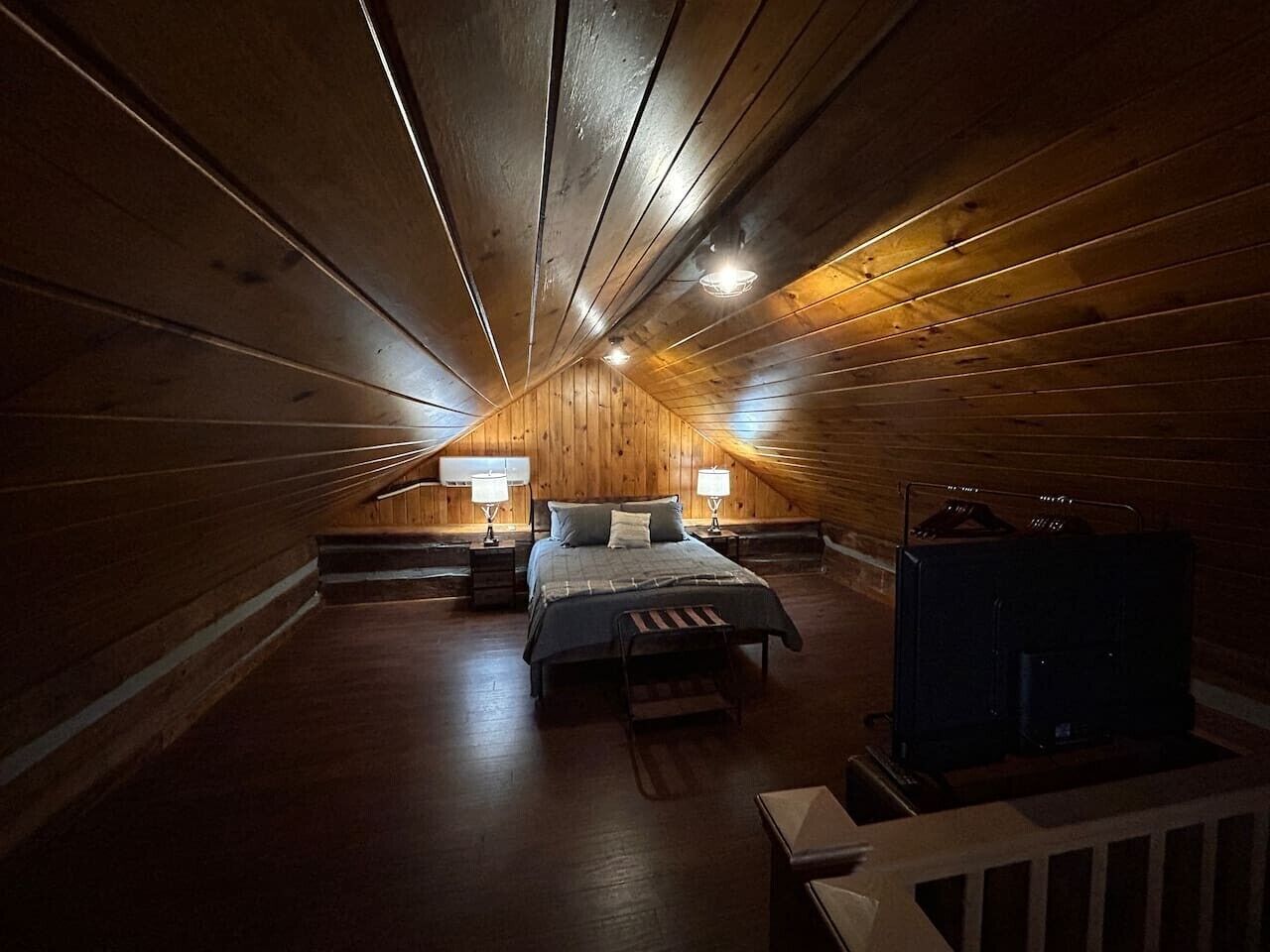 Une chambre confortable située dans les combles, avec un plafond en pente en bois, un lit avec une banquette, deux tables de chevet avec des lampes et un radiateur.