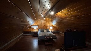 A cozy attic bedroom with a wooden sloped ceiling, a bed with a bench, two bedside tables with lamps, and a heater. - Garfield Place — Your Nature Escape Awaits! (Alpine)
