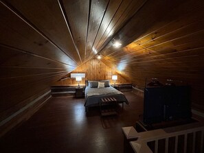 Ein gemütliches Schlafzimmer im Dachgeschoss mit schrägem Holzboden, einem Bett mit Sitzbank, zwei Nachttischen mit Lampen und einem Heizgerät.
