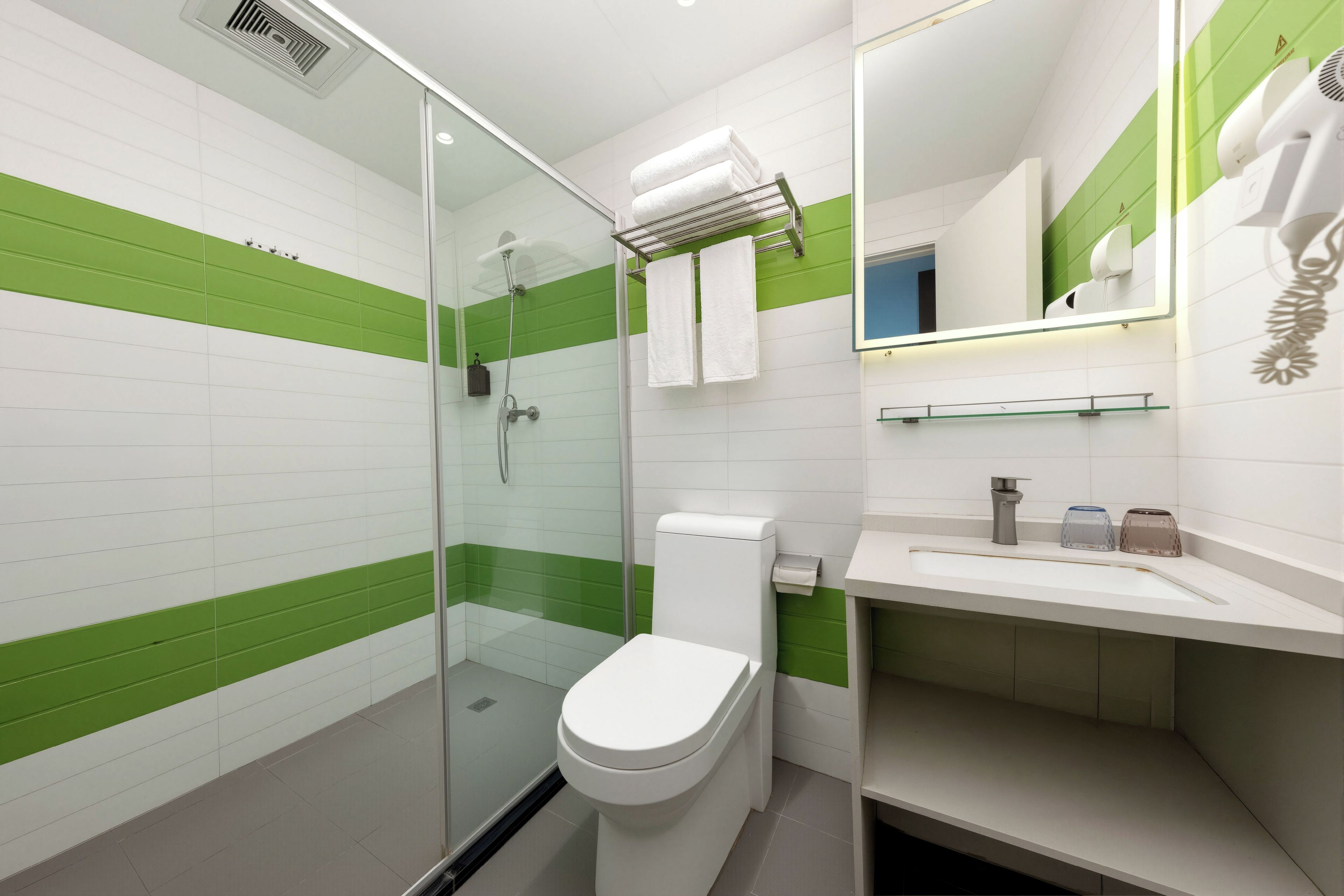 Un baño moderno con cabina de ducha de vidrio, inodoro blanco y lavamanos con espejo.