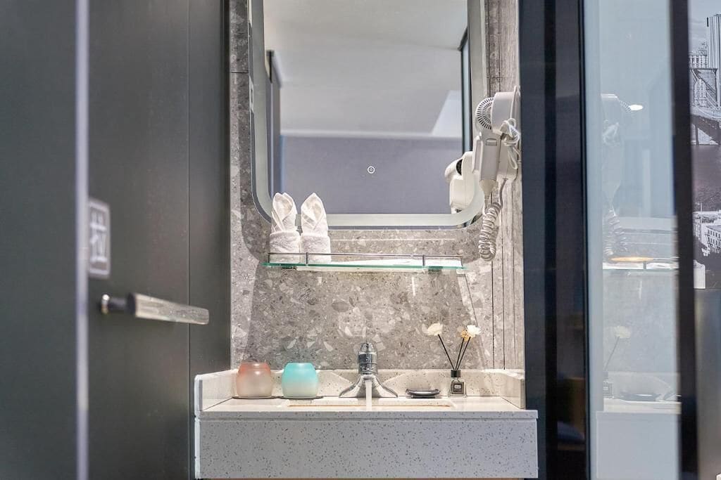 Un baño con espejo, lavamanos, secador de pelo y un par de pantuflas.