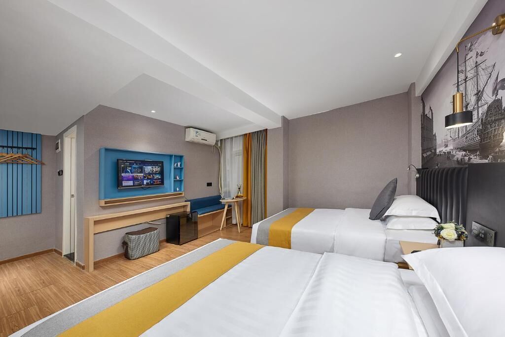 A hotel room with two beds, a desk, a TV, and a mural on the wall.