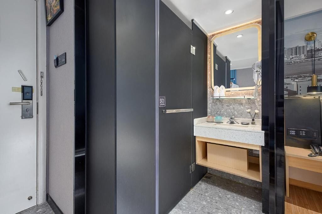A modern bathroom with a dark door, a sink with a marble countertop, and a mirror with a cityscape view.