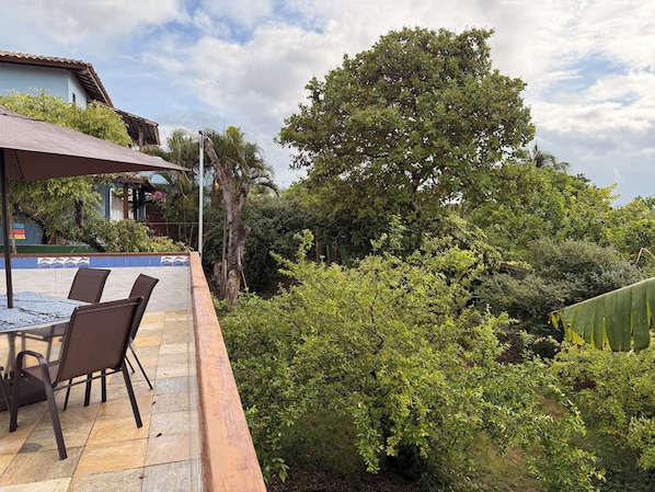 Un patio al aire libre con una mesa y sillas, rodeado de abundante vegetación y un gran árbol.