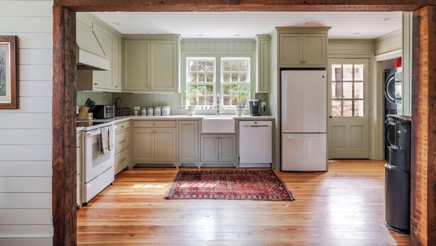 Una cocina con vigas de madera, armarios verde claro, un refrigerador blanco y una alfombra roja.