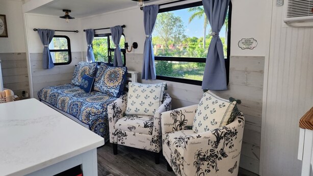 A cozy RV interior with a bed, two chairs, a table, and large windows with curtains. - 12 min to the Everglades Nat. Park & near FL Keys! Cozy RV in Redland w/laundry (Homestead)