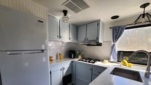 A compact kitchen with light blue cabinets, a white refrigerator, a gas stove, and a window with curtains. - 12 min to the Everglades Nat. Park & near FL Keys! Cozy RV in Redland w/laundry (Homestead)