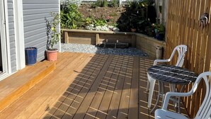 A wooden deck with a table and chairs, surrounded by a white fence and garden beds.