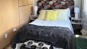A bedroom with a bed, bedside lamps, a bench, a patterned rug, and a window.