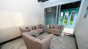 A living room with two beige sofas, a coffee table, and a large sliding glass door leading to a garden.