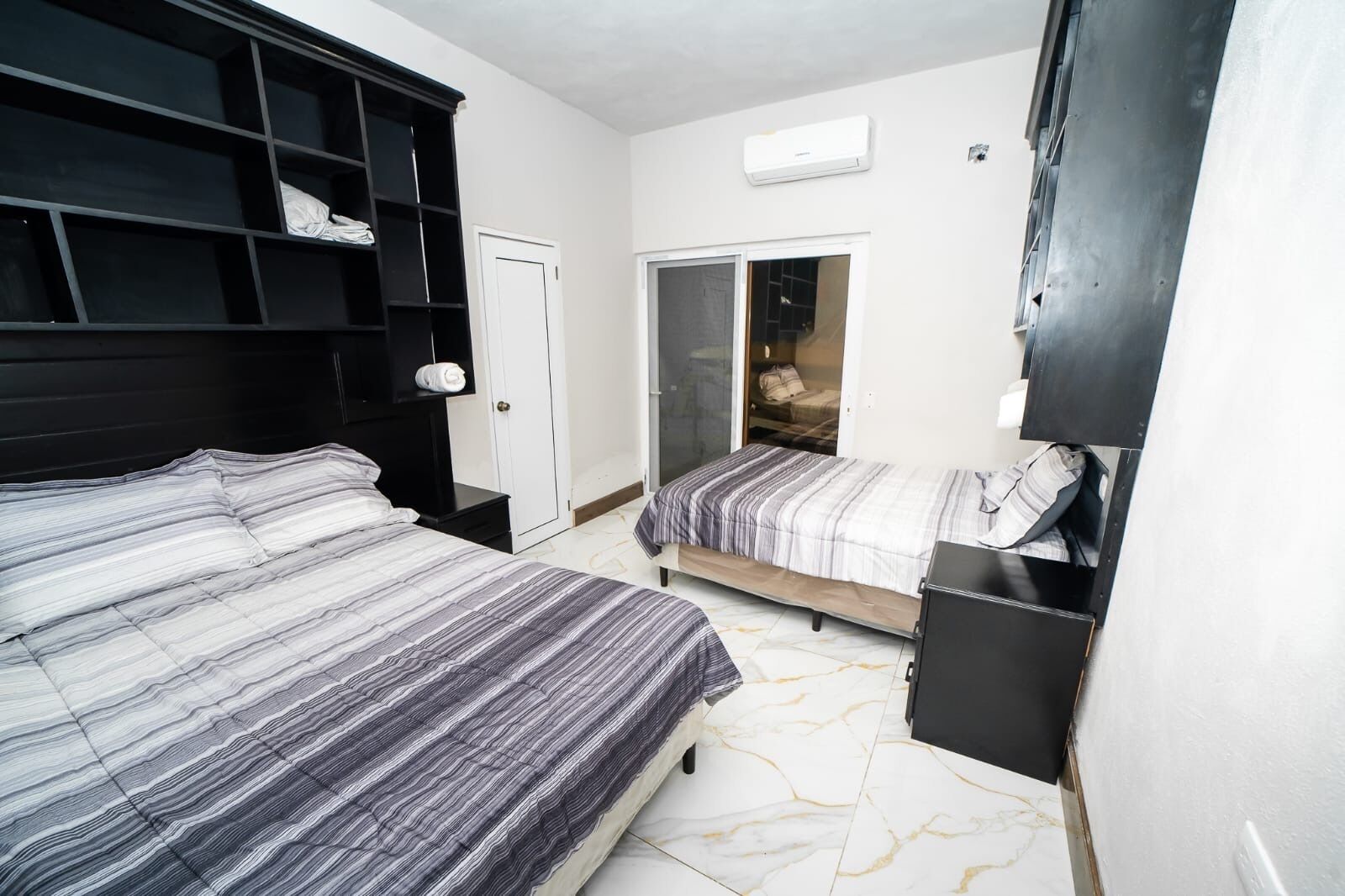 A bedroom with a bed, a wardrobe, a wardrobe with shelves, a door, and a window.