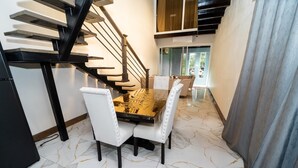 A dining area with a marble floor, a wooden table, and white upholstered chairs.