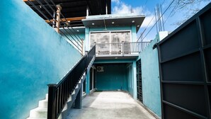 A narrow corridor with a staircase leading to a balcony, enclosed by walls painted in a single color.