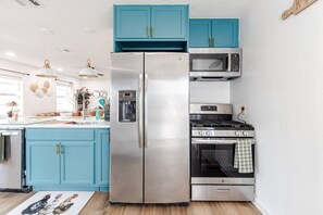 Una cucina con mobili color petrolio, un frigorifero in acciaio inossidabile, un forno a microonde e un piano cottura.