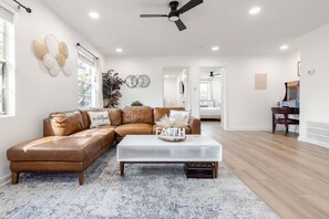 A spacious living room with a brown leather sectional sofa, a white coffee table with decorative items, and a wooden floor. - Renovated Brentwood Home Near DT, Domain & Q2 (Austin)