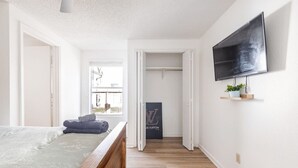 Un dormitorio con cama, piso de madera, televisor montado en la pared y armario con la puerta abierta.