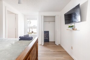 A bedroom with a bed, a wooden floor, a TV mounted on the wall, and a closet with a door open. - Renovated Brentwood Home Near DT, Domain & Q2 (Austin)