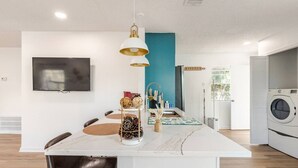 Una cocina moderna con lavadora incorporada, un comedor con una isla blanca y un televisor montado en la pared.