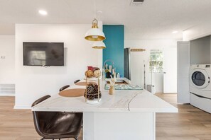 A modern kitchen with a built-in washing machine, a dining area with a white island, and a TV mounted on the wall. - Renovated Brentwood Home Near DT, Domain & Q2 (Austin)