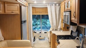 Een compacte camperkeuken met een eethoek, een ingebouwde koelkast, een magnetron en een fornuis.