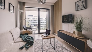 Een moderne woonkamer met een bank, een salontafel, een laptop, een televisie en een groot raam met uitzicht op gebouwen.