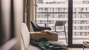 Een gezellige kamer met een bank, een stoel, een tafel en een groot raam met uitzicht op gebouwen.