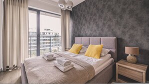 Een moderne slaapkamer met een groot bed, een nachtkastje, een lamp en uitzicht op de stad door grote ramen.