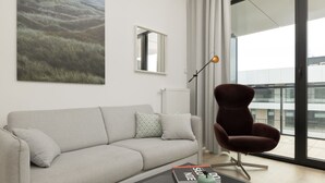 Una sala de estar moderna con un sofá, una silla, una mesita de centro, un libro y un ventanal grande.