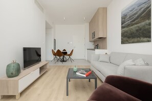 A modern living room with a flat-screen TV, a coffee table with a book, a sofa, and a dining area with chairs. - Oaza Spokoju Widok na Las Design Shellter (Trzebiatow)