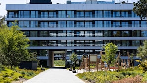 A modern multi-story building with a central entrance, surrounded by greenery and a paved walkway. - Widok na Morze Przy Pla y Taras Shellter (Trzebiatow)