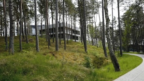 A modern building with a sloped roof, surrounded by a forested area with a paved path. - Widok na Morze Przy Pla y Taras Shellter (Trzebiatow)