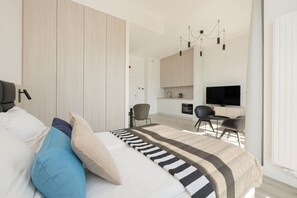 Ein modernes Schlafzimmer mit Bett, Fernseher, Schreibtisch und einer Küchenzeile.