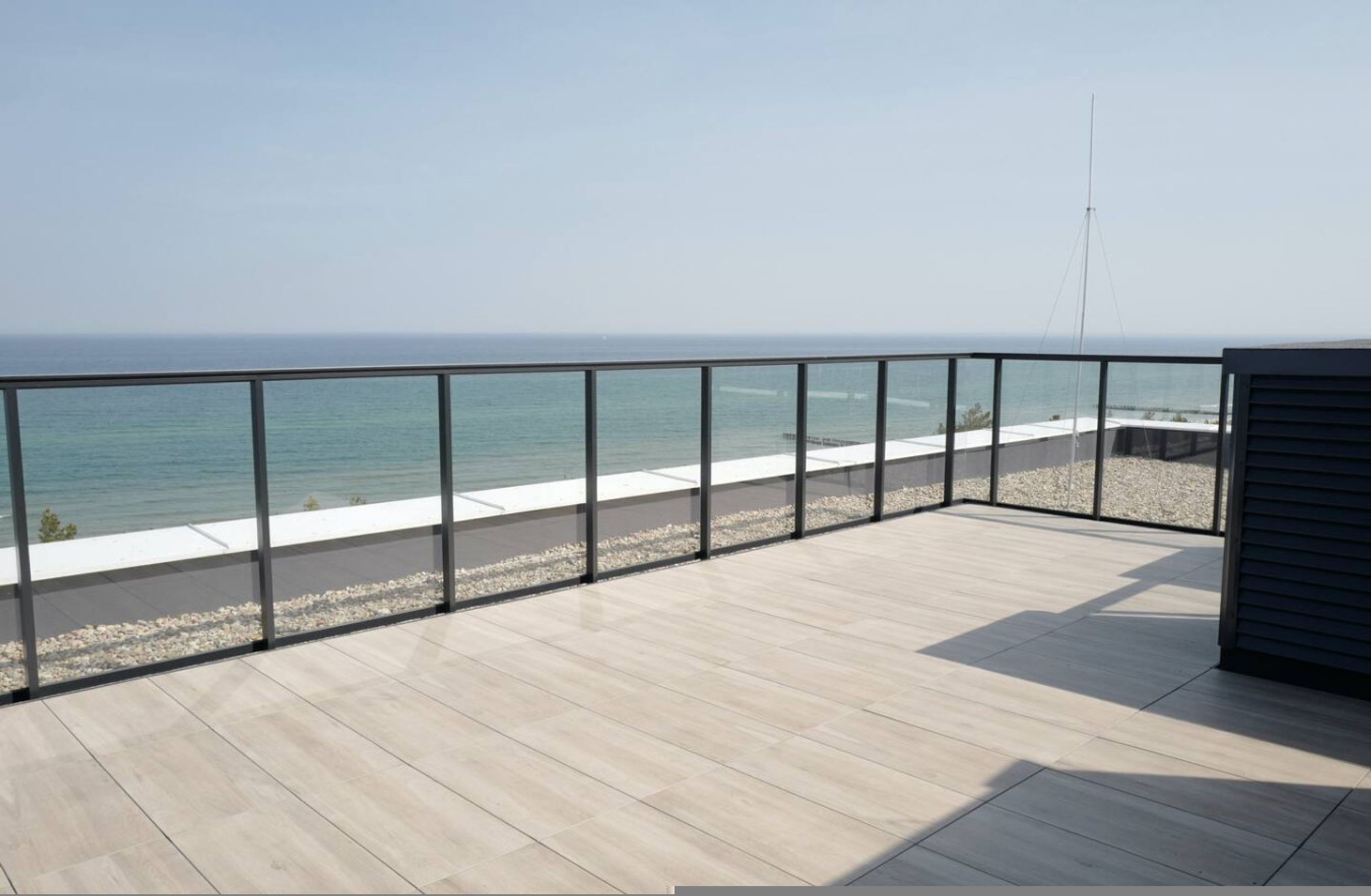 A balcony with a view of the sea, a railing, and a building with a sloped roof.