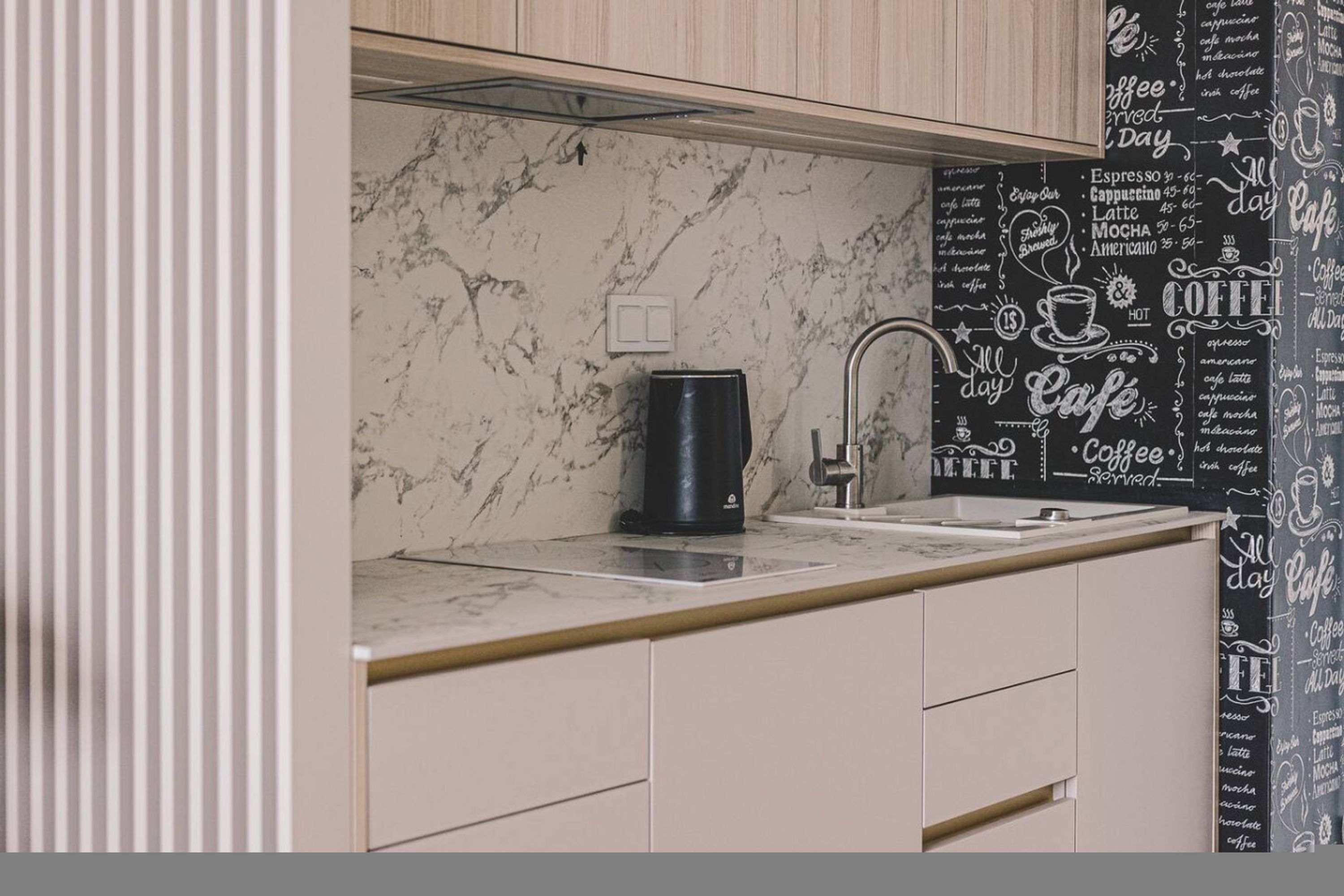 A kitchen with marble countertops, a coffee maker, and a black backsplash with coffee-related text.