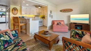 A living room with a sofa, a coffee table, a television, and a kitchen area with cabinets and a microwave. - Casa De Emdeko 303 | Ocean View | Central AC (Kailua Kona)