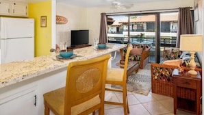 A compact kitchen with a dining area, a television, and a view of the outside. - Casa De Emdeko 303 | Ocean View | Central AC (Kailua Kona)