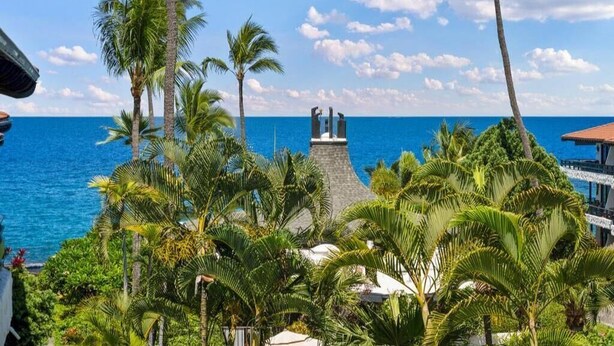A tropical resort with a view of the ocean, palm trees, and a statue. - Casa De Emdeko 303 | Ocean View | Central AC (Kailua Kona)