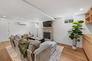 A living room with a fireplace, a sofa set, a coffee table, and a large potted plant. - Large Clean & Modern Basement Apartment Near Aggie (Manhattan)