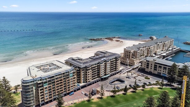 Ein Hotel an der Küste mit Blick auf den Strand, inklusive Parkplatz und einem Yachthafen.