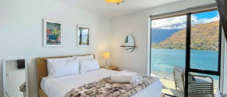 Un dormitorio con una cama grande, vista a un lago y una montaña al fondo.