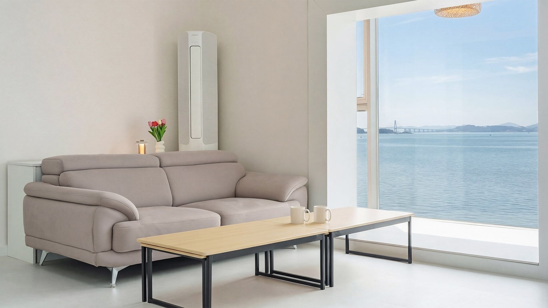 A modern living room with a sofa, a coffee table, and a view of a body of water through a large window.
